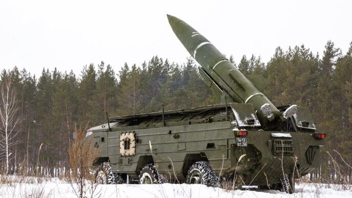 A Soviet OTR-21 Tochka tactical ballistic missile is mounted on its large, multi-wheeled military launcher vehicle, angled upwards in a snowy, forested landscape.