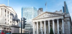 A low-angle shot looking up at the grand, historical facade of the Bank of England in London, emphasizing its classical architecture and imposing columns.