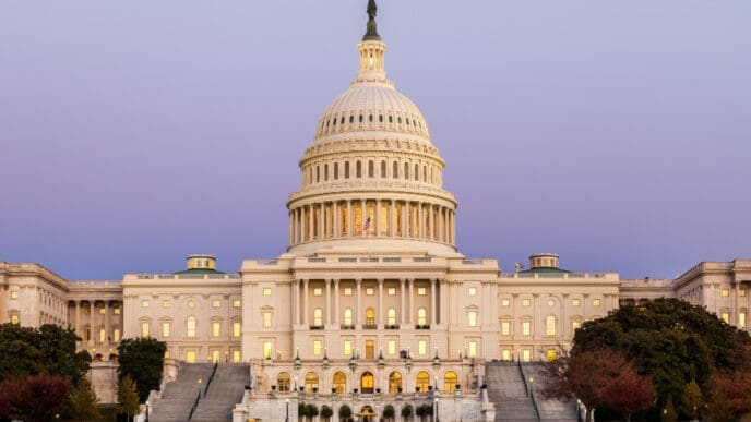 The U.S. Capitol Building in Washington, D.C., is brightly illuminated at dusk, showcasing its iconic dome, grand steps, and classical architecture against a purple and blue twilight sky.
