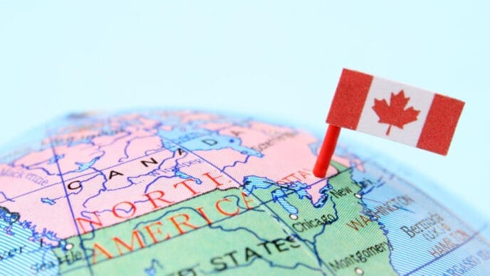 A close-up photograph of a globe showing the map of North America, with the border between Canada and the United States prominently visible. A Canadian flag is pinned into the map near this border, symbolizing cross-border trade.