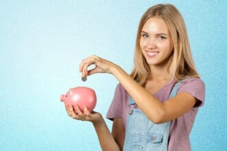 A smiling young woman putting a coin into a pink piggy bank.