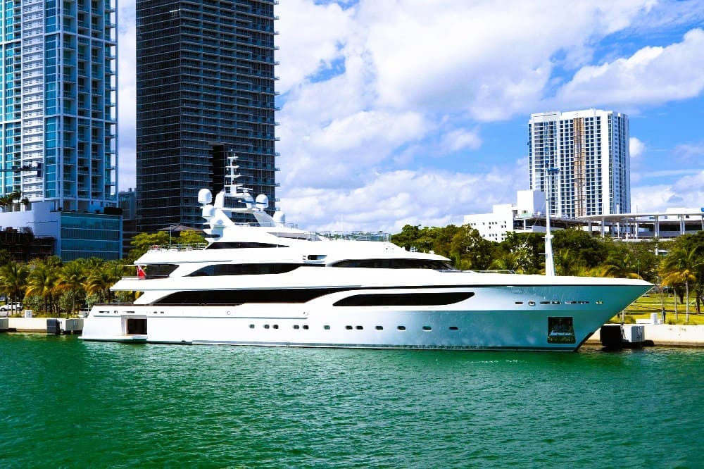 A large white superyacht docked in Biscayne Bay, with the downtown Miami skyline and palm trees in the background.