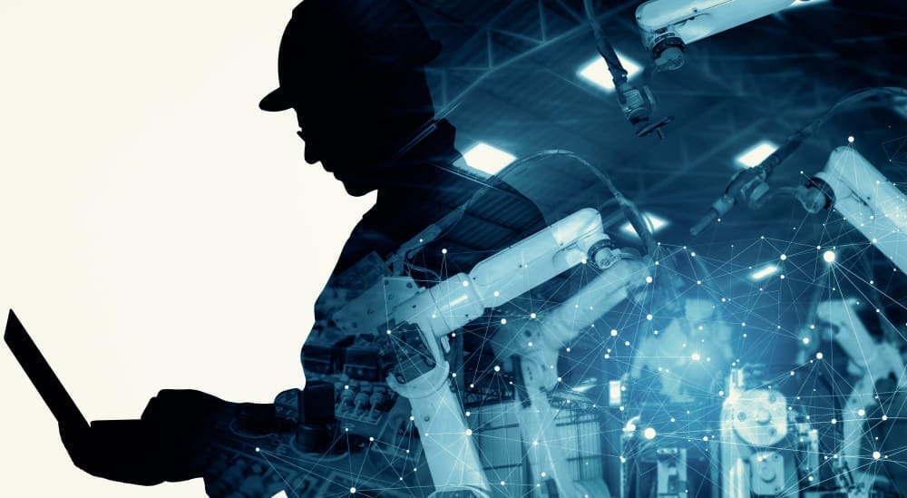 A silhouette of an engineer in a hard hat working on a laptop, overlaid with a blue-toned digital network and robotic arms, symbolizing AI's disruption of industrial sectors.