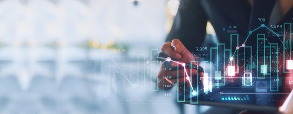 A person in a dark suit interacts with a holographic digital display showing various financial graphs, bar charts, and data, indicating analysis and problem-solving in a FinTech context.