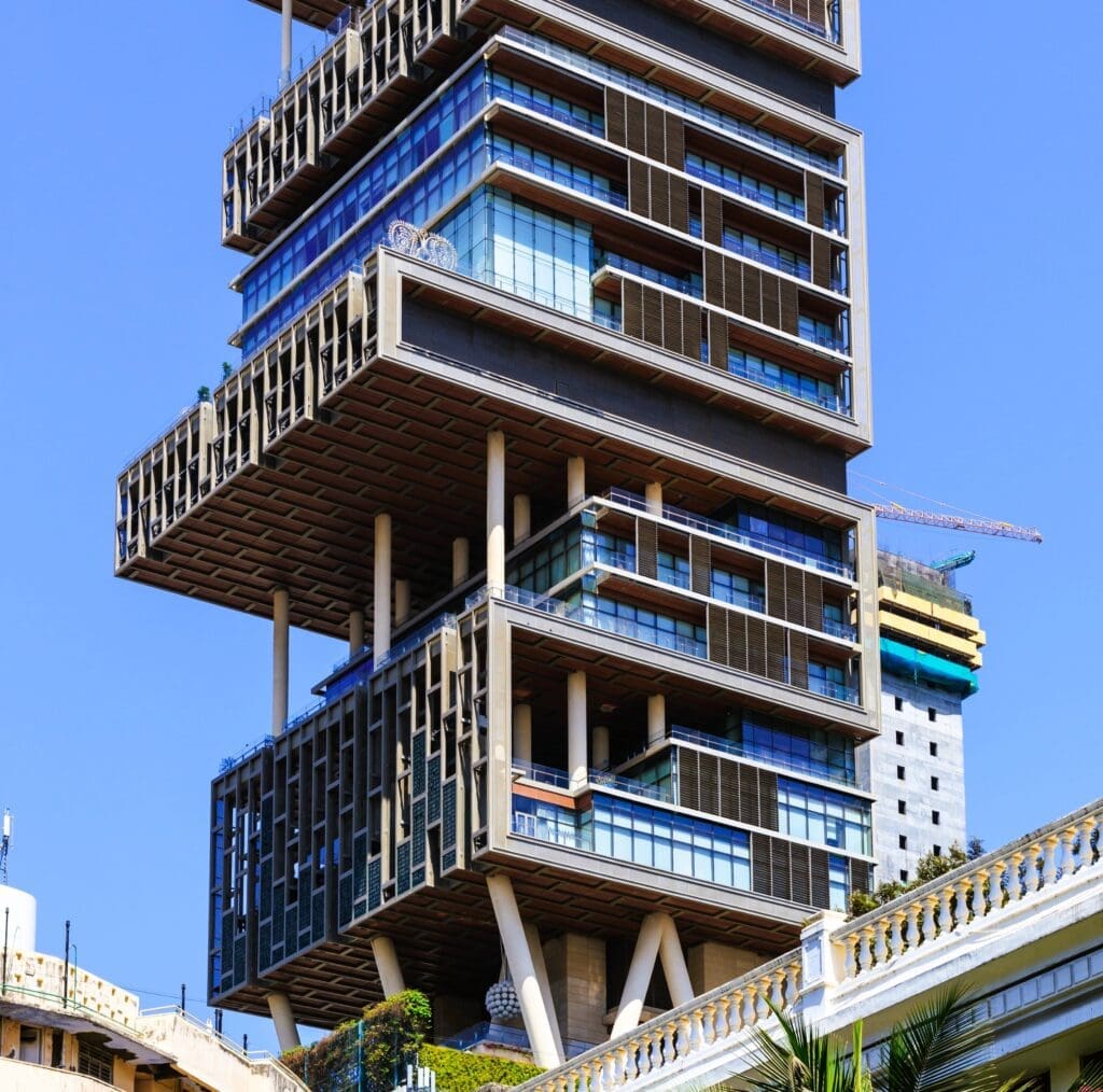 A low-angle view of Antilia Tower in Mumbai, India, a unique skyscraper with alternating floors and large cantilevered sections.