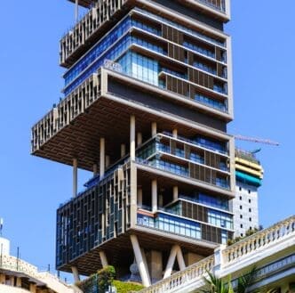 A low-angle view of Antilia Tower in Mumbai, India, a unique skyscraper with alternating floors and large cantilevered sections.