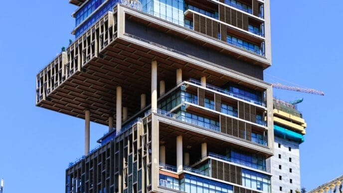A low-angle view of Antilia Tower in Mumbai, India, a unique skyscraper with alternating floors and large cantilevered sections.