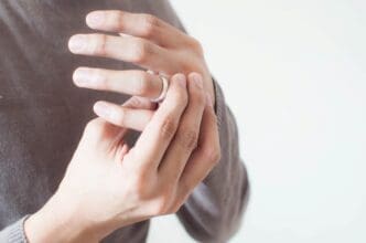 A close-up of a person's hands, with one hand adjusting or removing a plain silver ring from a finger of the other hand, against a white background.