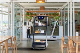 An autonomous waiter robot with multiple shelves carrying food and drinks, operating in a modern, brightly lit restaurant.