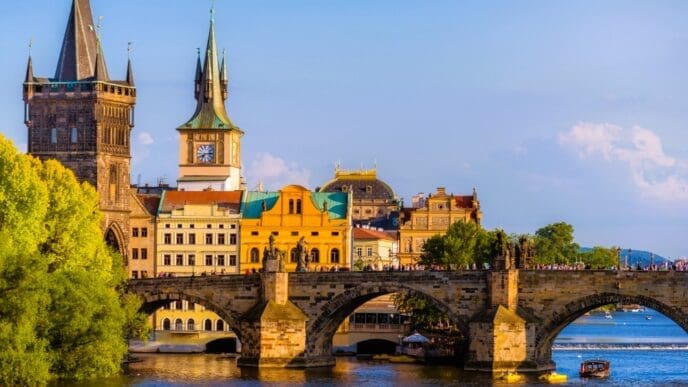 The Charles Bridge in Prague, adorned with statues and towers, spanning the Vltava River, with historic buildings under a blue sky.