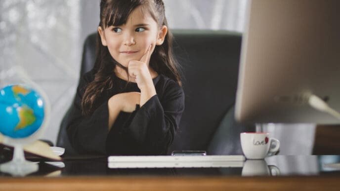 A young girl with dark hair and bangs, wearing a black shirt, sits at a large desk with a computer monitor, globe, and mug, looking thoughtfully to the side with her hand on her chin.