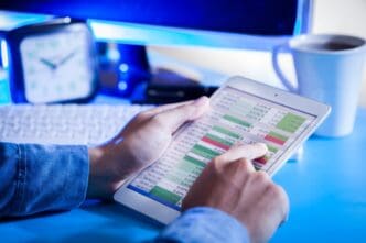 A close-up of a person's hands holding a digital tablet that displays a complex financial spreadsheet or budgeting data, with a finger touching the screen.