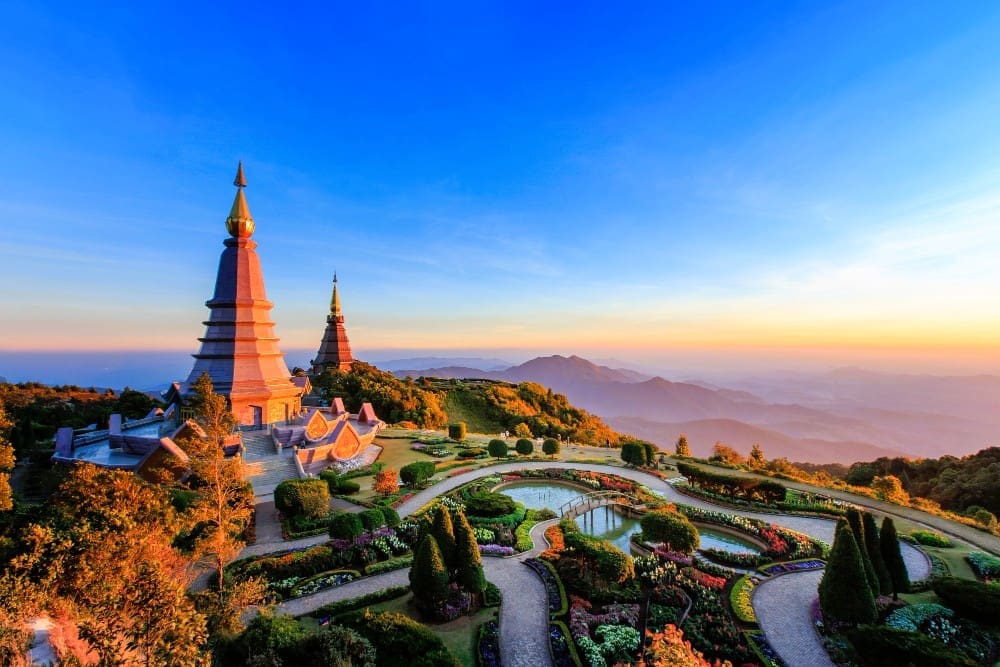 The Phra Mahathat Naphamethanidon and Naphapholphumisiri pagodas in Doi Inthanon National Park, Thailand, surrounded by ornate gardens and mountains at sunset.