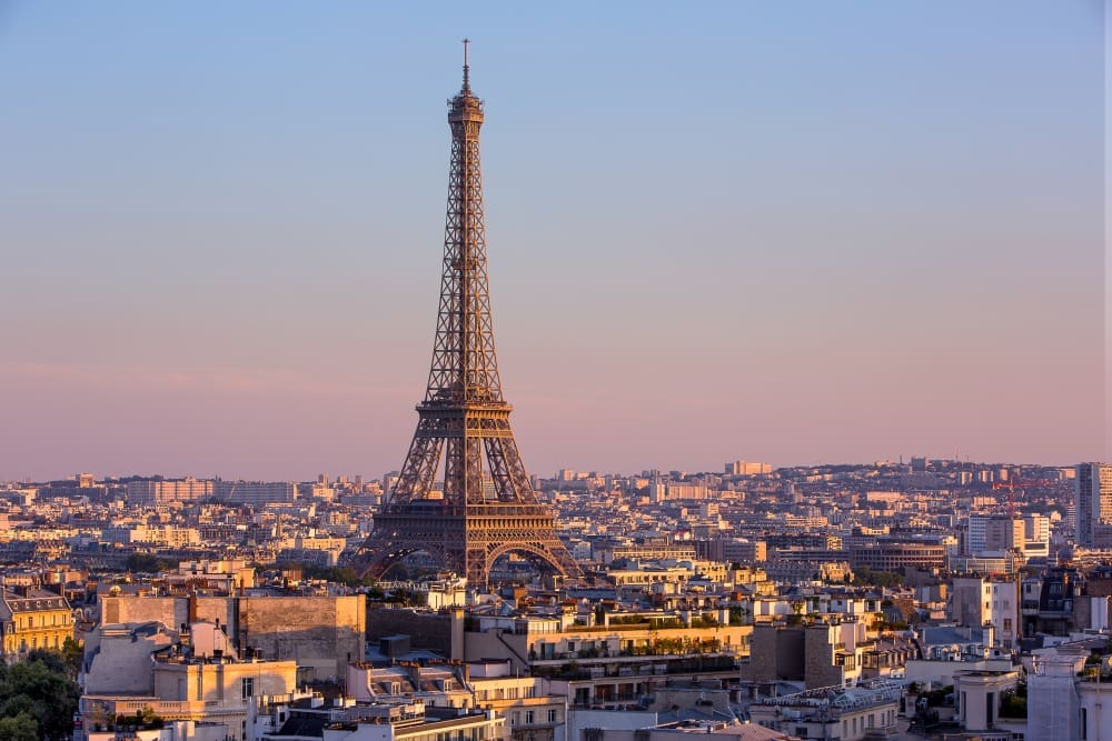 The iconic Eiffel Tower stands tall over the sprawling Parisian cityscape, bathed in the soft, warm light of sunrise or sunset under a pastel sky.