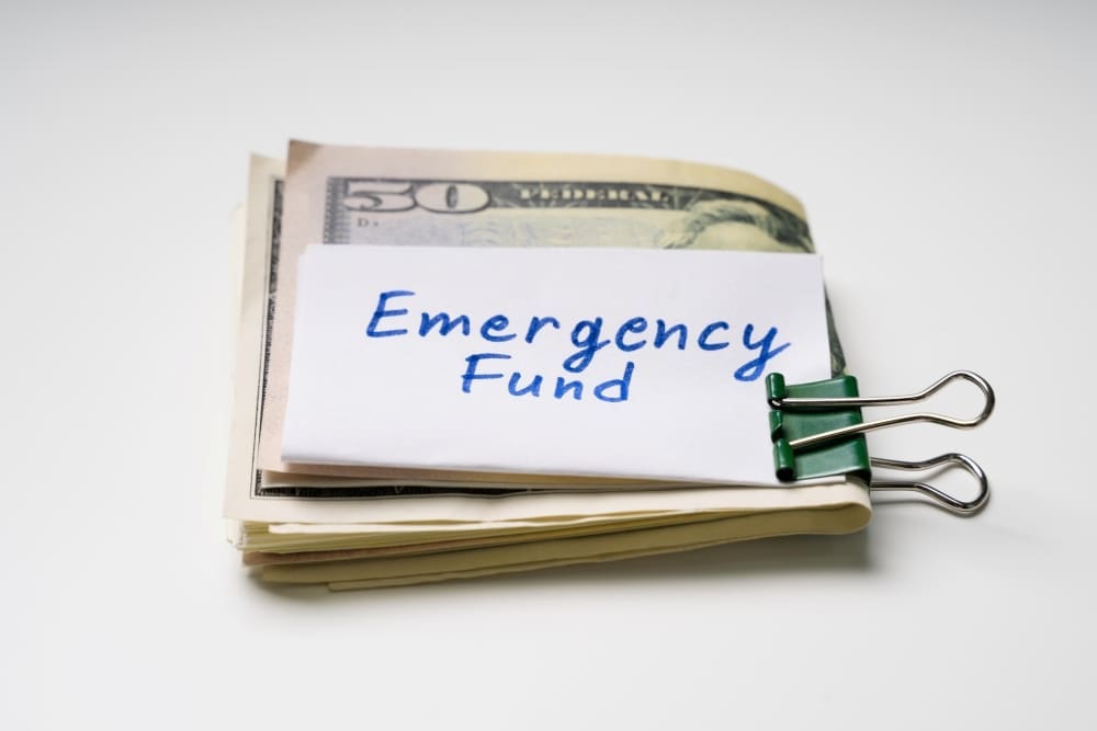 A stack of US dollar bills with a note reading "Emergency Fund" clipped to it.
