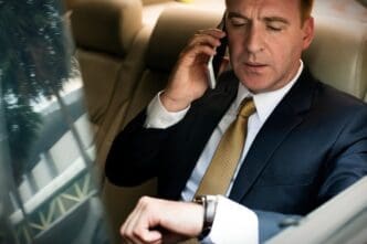 A businessman in a suit making a phone call in a car, checking his watch, conveying busy time management.