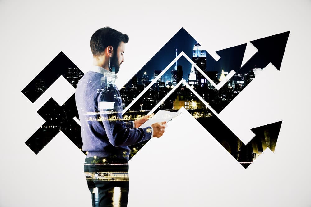 A double exposure image of a man holding papers, superimposed with an upward-trending arrow and a cityscape at night, symbolizing financial growth.