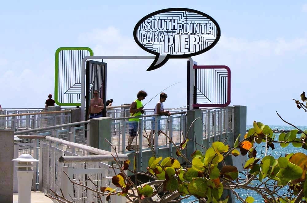 People fishing on South Pointe Park Pier in Miami Beach, with the "SOUTH POINTE PARK PIER" sign overhead.