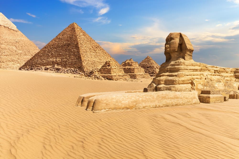 The Great Sphinx of Giza with the Pyramids in the background, set against a blue sky over the desert.