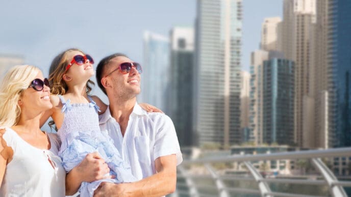 A happy family, including a mother, father, and young daughter, smiling and looking up, with a city skyline in the background.