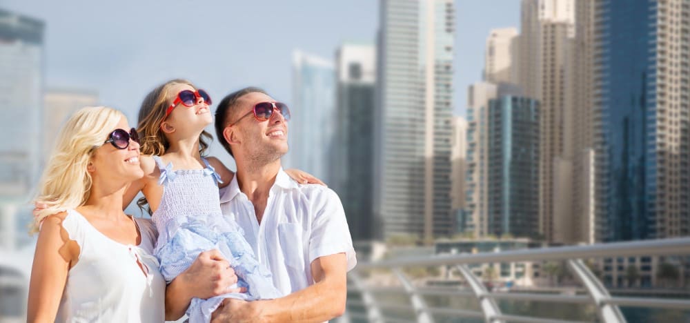 A happy family, including a mother, father, and young daughter, smiling and looking up, with a city skyline in the background.