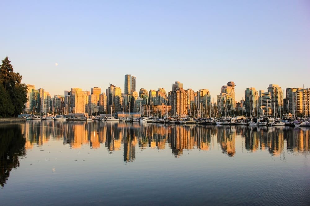 The vibrant skyline of downtown Vancouver, Canada, reflecting in the calm waters of the harbor, with numerous boats docked.