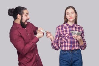 A man eagerly trying to take money from a woman who looks unimpressed, against a grey background.