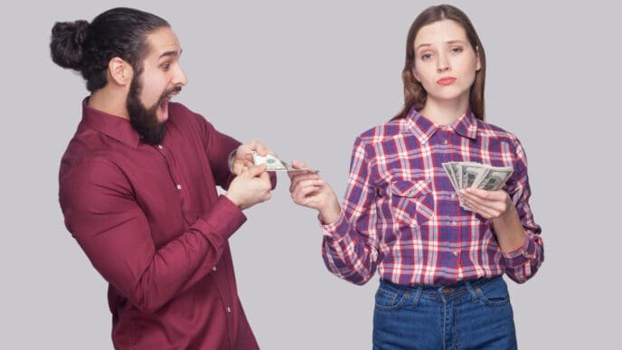 A man eagerly trying to take money from a woman who looks unimpressed, against a grey background.