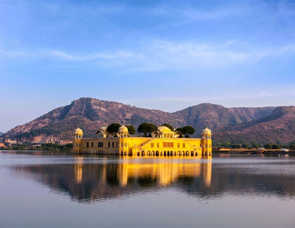 The golden yellow Jal Mahal (Water Palace) floating in Man Sagar Lake, with mountains in the background, in Jaipur, India.