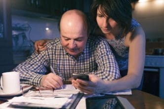A concerned couple reviewing documents and a smartphone, appearing to manage finances.