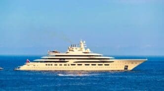 A massive beige mega yacht with a helicopter on its deck, moored in the sea on a sunny day.