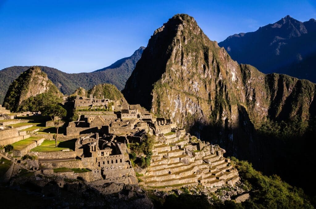 A close-up view of the ancient Inca stone walls and terraces of Machu Picchu, with dramatic mountains in the background under a clear sky.