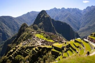 An elevated view of the ancient Inca city of Machu Picchu, with its terraces and structures, surrounded by dramatic green mountains under a clear sky.