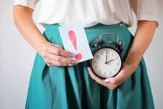 A woman holding an alarm clock and a card with an exclamation mark, symbolizing time and warning related to female health.