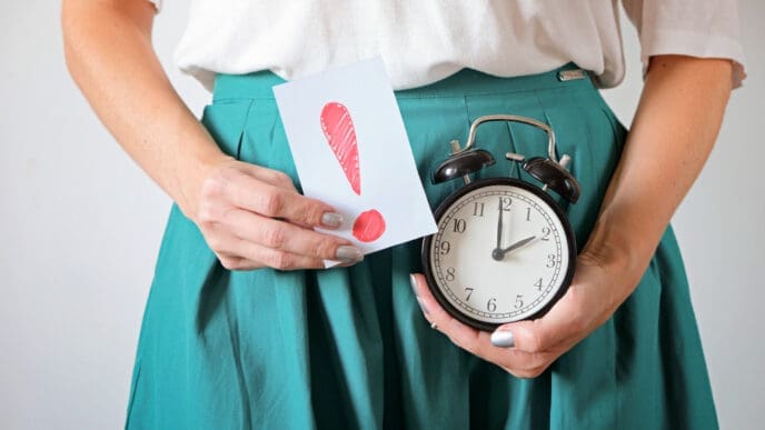 A woman holding an alarm clock and a card with an exclamation mark, symbolizing time and warning related to female health.