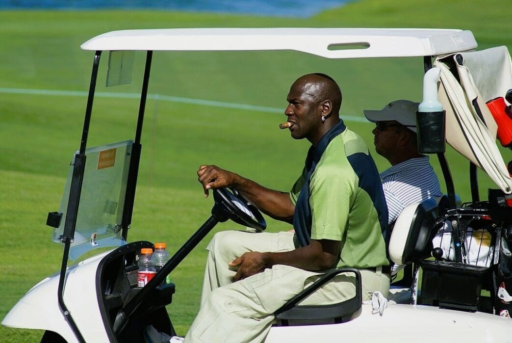 Michael Jordan driving a golf cart and smoking a cigar on a golf course.