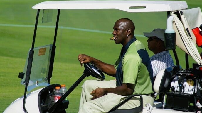 Michael Jordan driving a golf cart and smoking a cigar on a golf course.