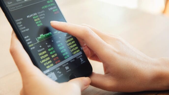 Close-up of hands holding a smartphone displaying a financial trading app with stock market data and charts.