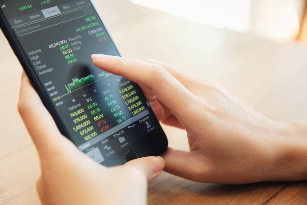 Close-up of hands holding a smartphone displaying a financial trading app with stock market data and charts.