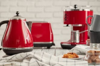 A red electric kettle, toaster, and coffee machine on a kitchen counter, with cookies and mugs.