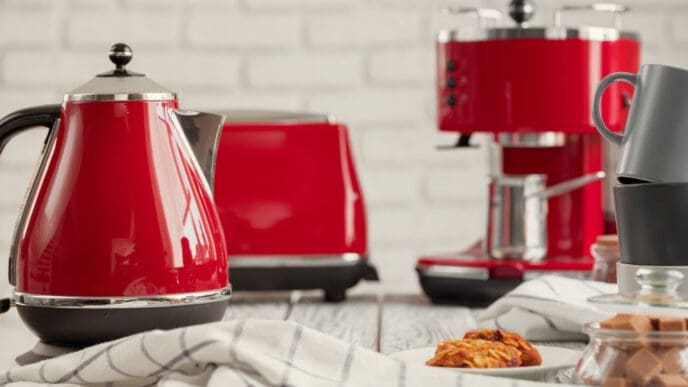 A red electric kettle, toaster, and coffee machine on a kitchen counter, with cookies and mugs.