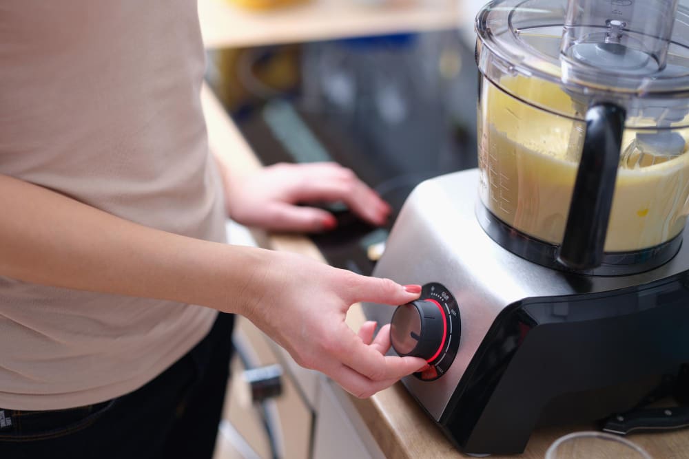 A close-up of a hand adjusting the dial of a food processor containing a light-colored mixture.