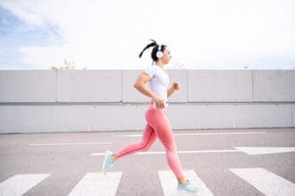 A woman in activewear and headphones running across a crosswalk outdoors, illustrating physical activity.