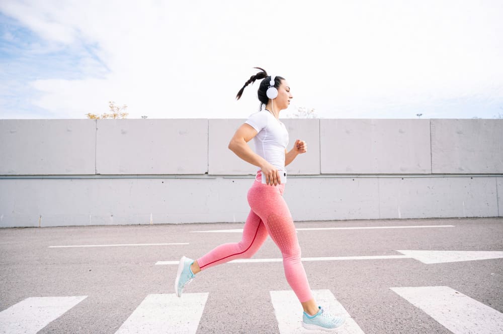 A woman in activewear and headphones running across a crosswalk outdoors, illustrating physical activity.
