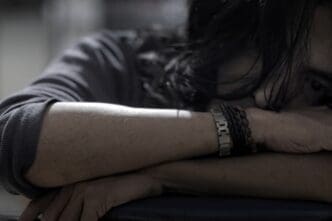 Close-up of a man with long hair, head down on his arms, appearing depressed or in distress.