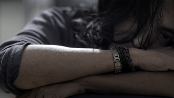 Close-up of a man with long hair, head down on his arms, appearing depressed or in distress.