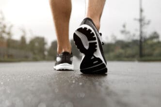 Close-up of a person's feet in black and white running shoes walking on a wet paved surface, seen from behind.