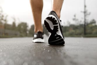 Close-up of a person's feet in black and white running shoes walking on a wet paved surface, seen from behind.