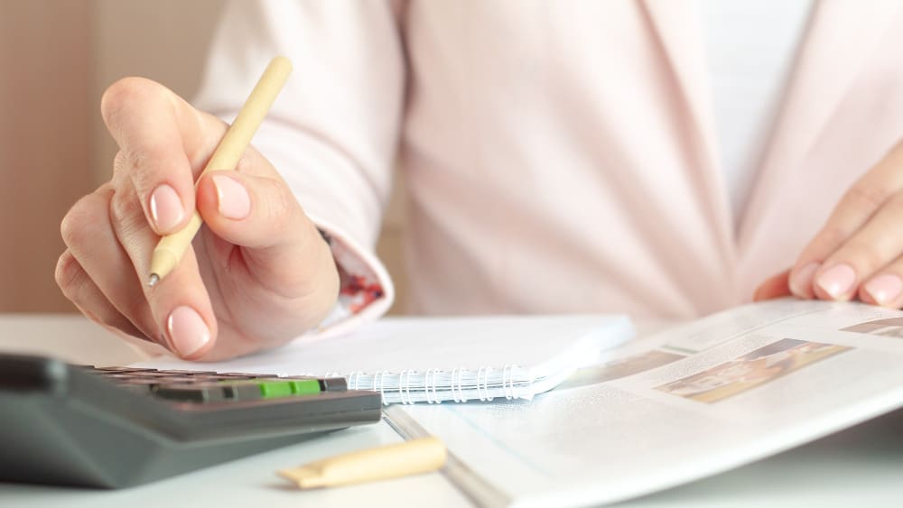 A close-up of a person's hands writing in a notebook with a pen while simultaneously using a calculator, symbolizing financial planning and budgeting.