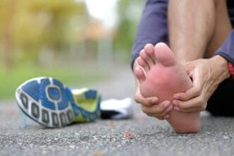 Close-up of a person holding their foot, indicating pain, with a running shoe nearby.